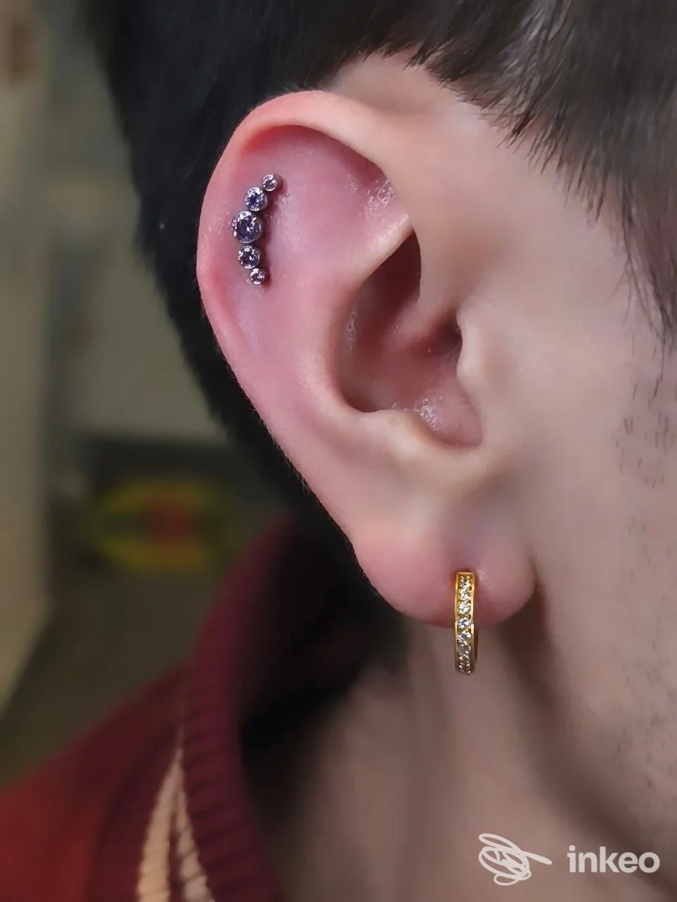 Orecchio di lato con tre piercing gialli intagliati e una barra nel lobo, piercing visibile su orecchio sinistro e una seconda al bordo dell’elice.