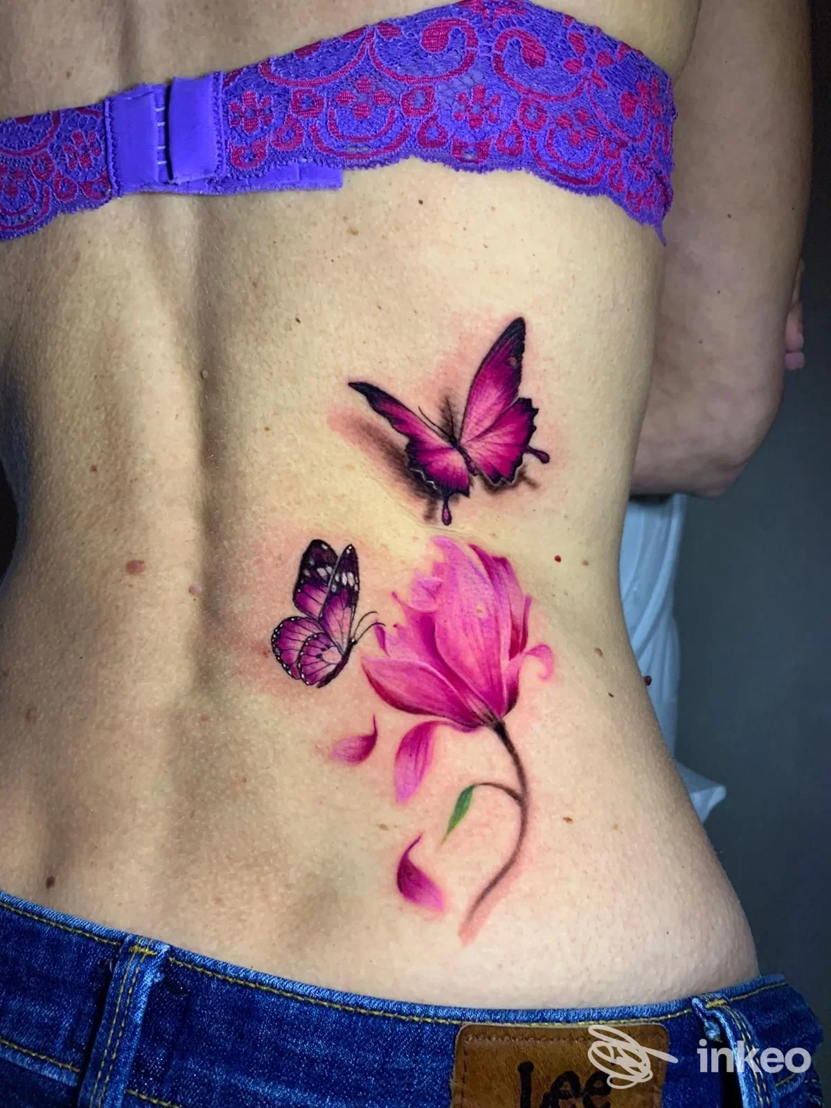 Tattoo colorato su pelle nella zona lombare, raffigurante due farfalle e un fiore rosa; visibile solo la schiena e parte della vita. Studio Malavida Tattoo.