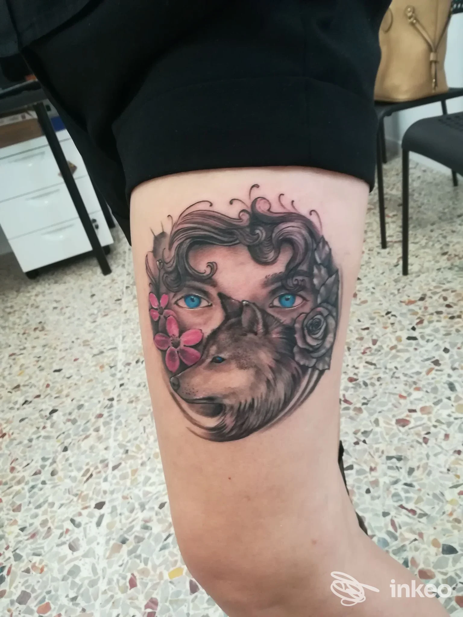 Tatuaggio realistico su gamba raffigurante un lupo con fiori rosa e dettagli floreali, realizzato sulla pelle.