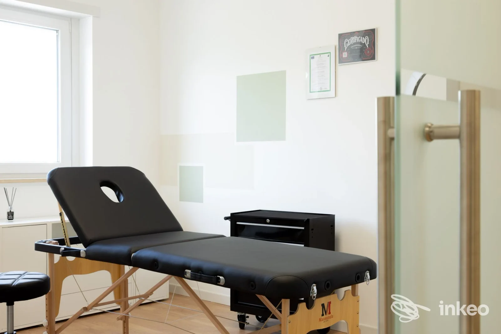 Foto di una postazione per tatuaggi in uno studio chiamato Minimal a L'Aquila: letto da tatuaggio nero, sedia, ambiente luminoso e ordinato.