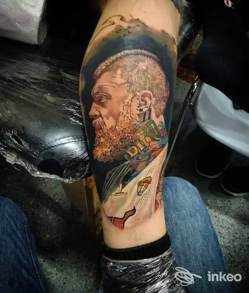 Tatuaggio realizzato su pelle della gamba raffigurante profilo di uomo ricco di barba, colori vivaci e dettagli realistici.