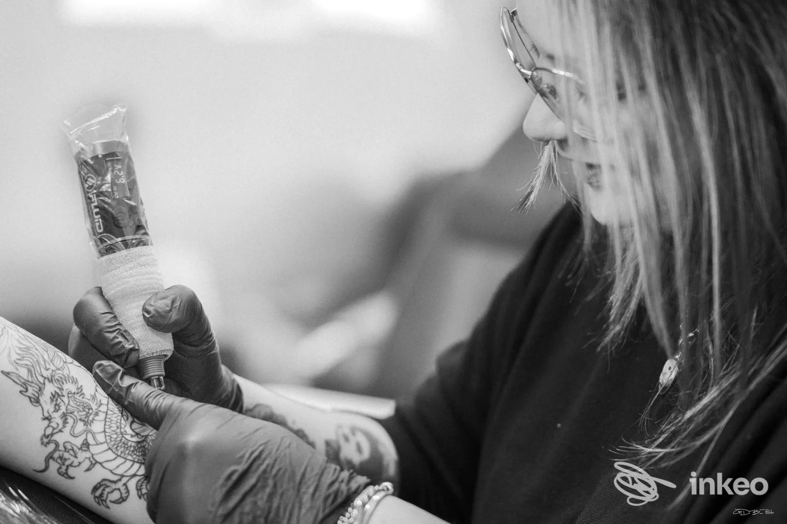 Praticante tatuando braccio con guanti, disegno in corso su pelle, immagine in bianco e nero. The Silver Rose Tattoo Shop, Cepagatti.