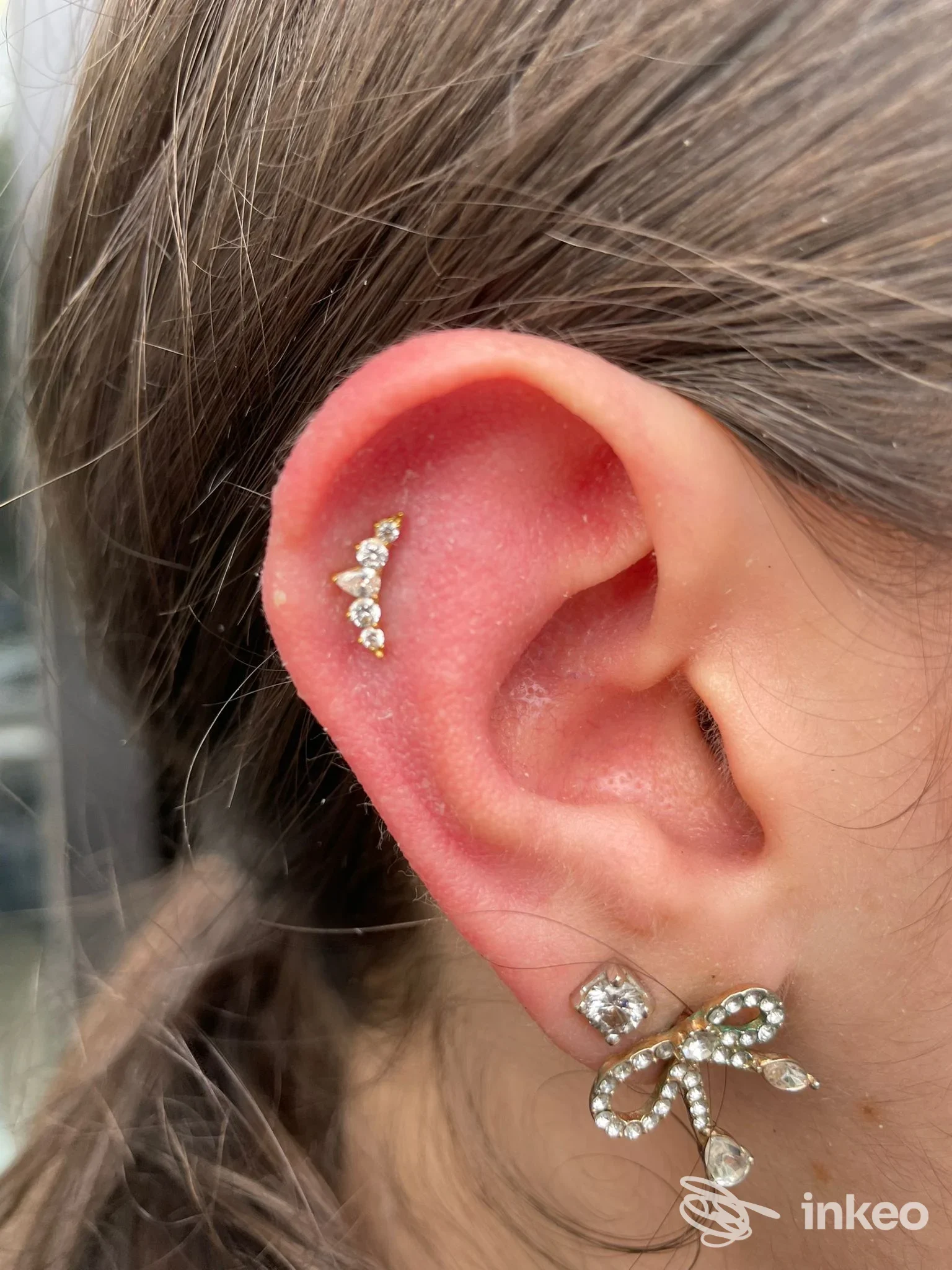 Orecchio sinistro con due piercing: una cerniera dorata con pietre lungo l’anthelix e una piccola orecchino a clip sulla lobule, gioielli luminosi.