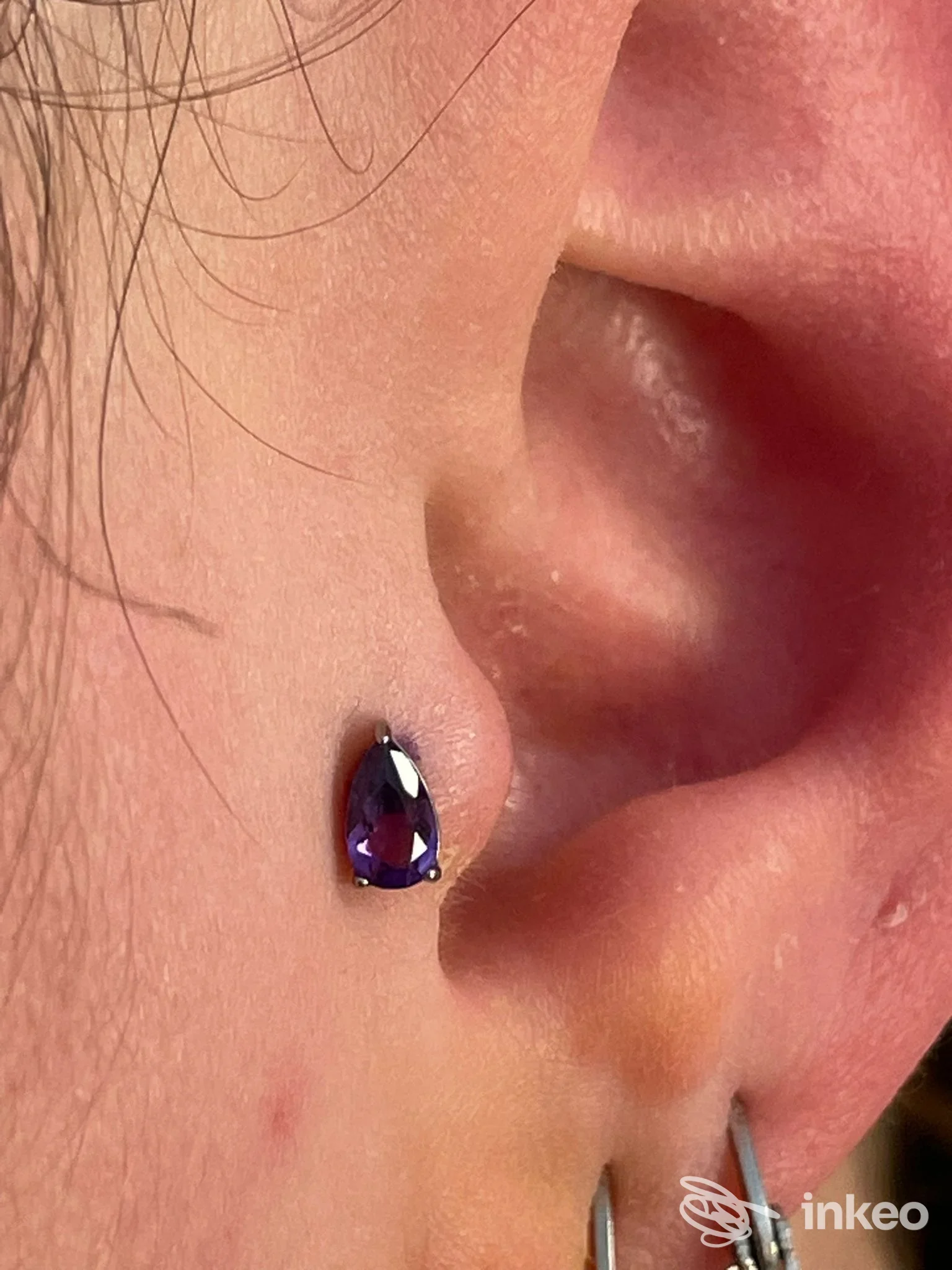 Piercing all’orecchio con gioiello a goccia viola, visibile su pelle reale; studio Freehand Fucktory Tattoo & Piercing, Mosciano Sant’Angelo.
