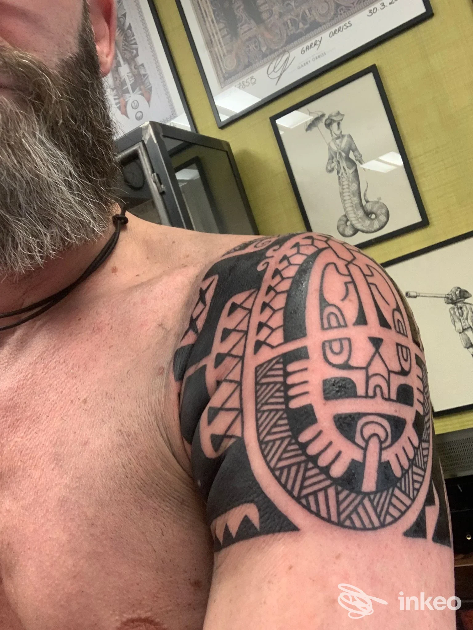 Parte superiore del braccio e della spalla di un uomo con un tattoo nero tribale su pelle chiara, sfondo con stampe artistiche nello studio di Milano.