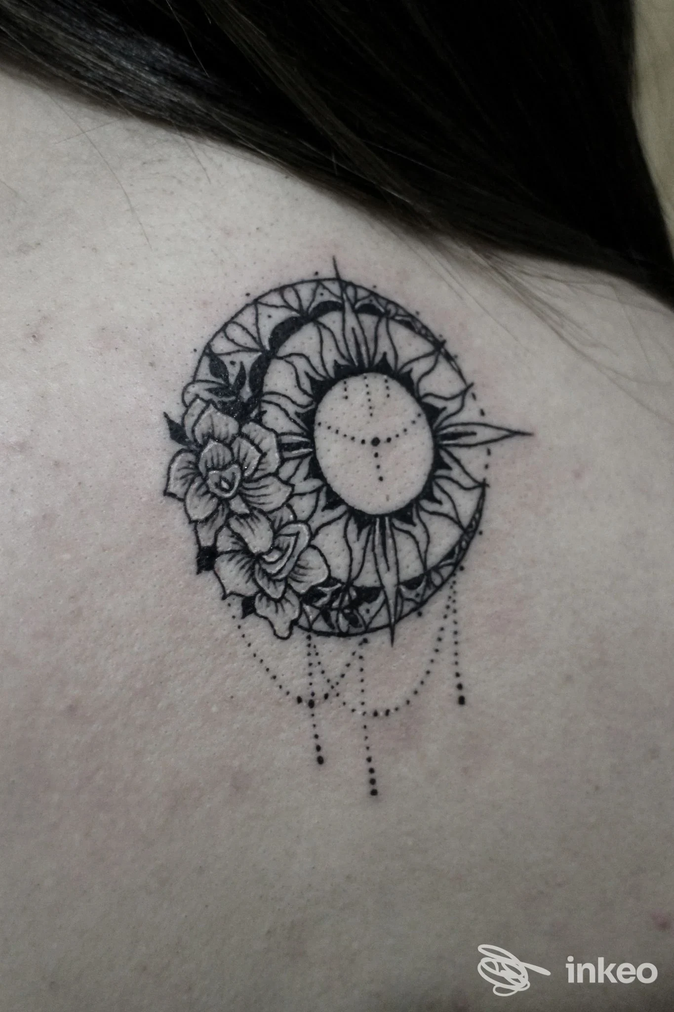 Tattoo circolare con fiori e pendenti a cascata, eseguito sulla pelle, stile line-work e floral mandala, in bianco e nero.