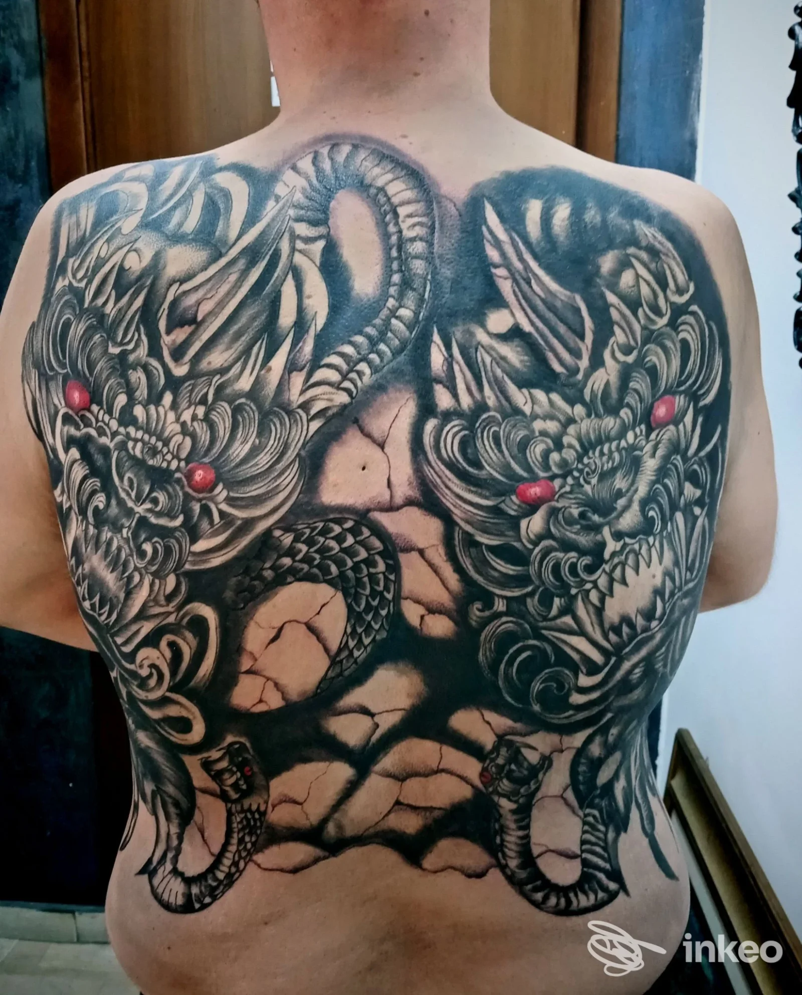 Schiena di un uomo con tatuaggio completo di draghi e motivi intricati in tonalità nero-grigio, visibile dalla nuca ai fianchi, senza volti o elementi visibili di un volto.