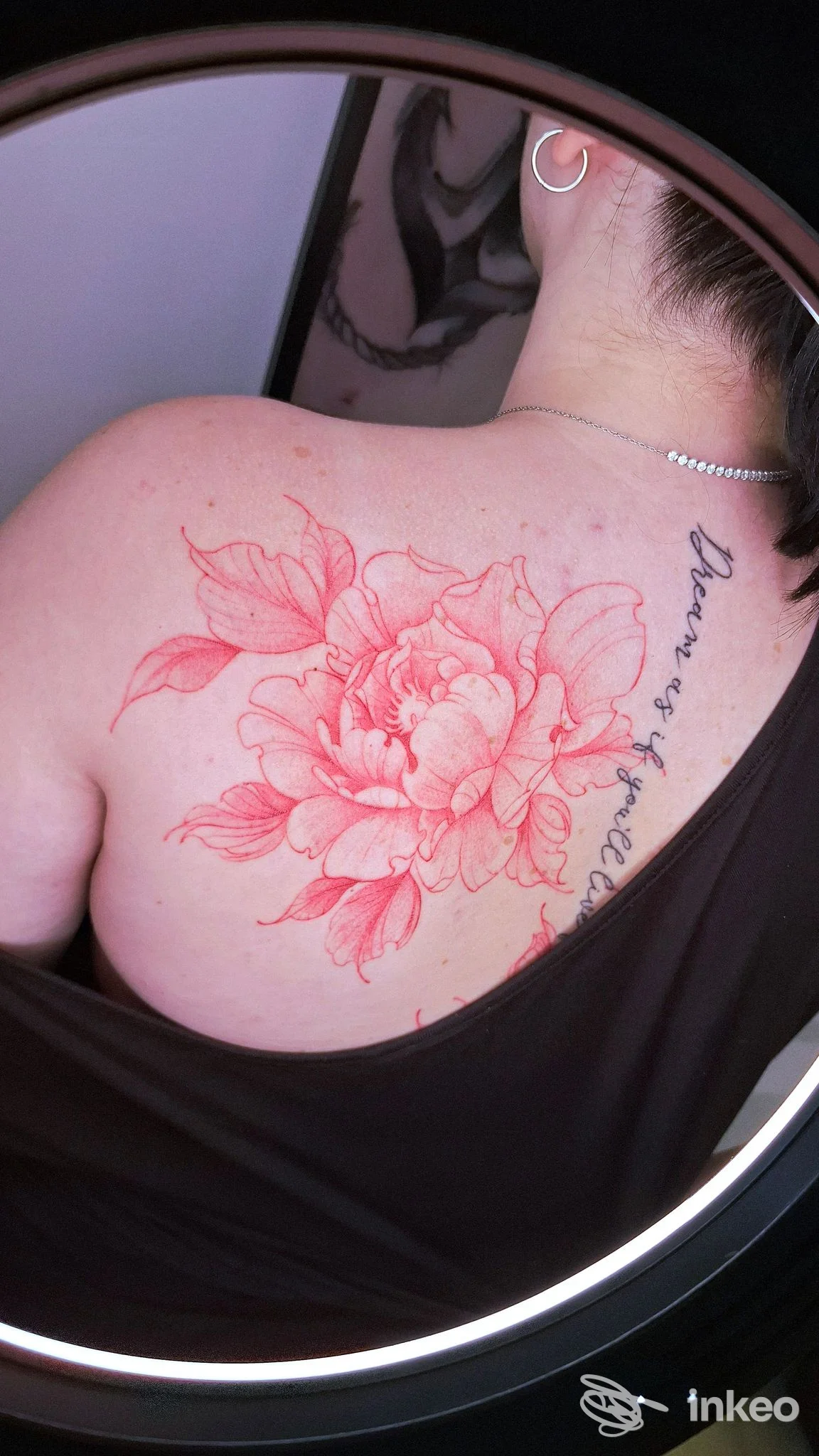 Tattoo floreale in rosso sulla spalla di una persona, con scritte lungo la schiena, visibile in primo piano su pelle nuda; scatto in cornice rotonda, studio New Moon Tattoo Studio, Chieti