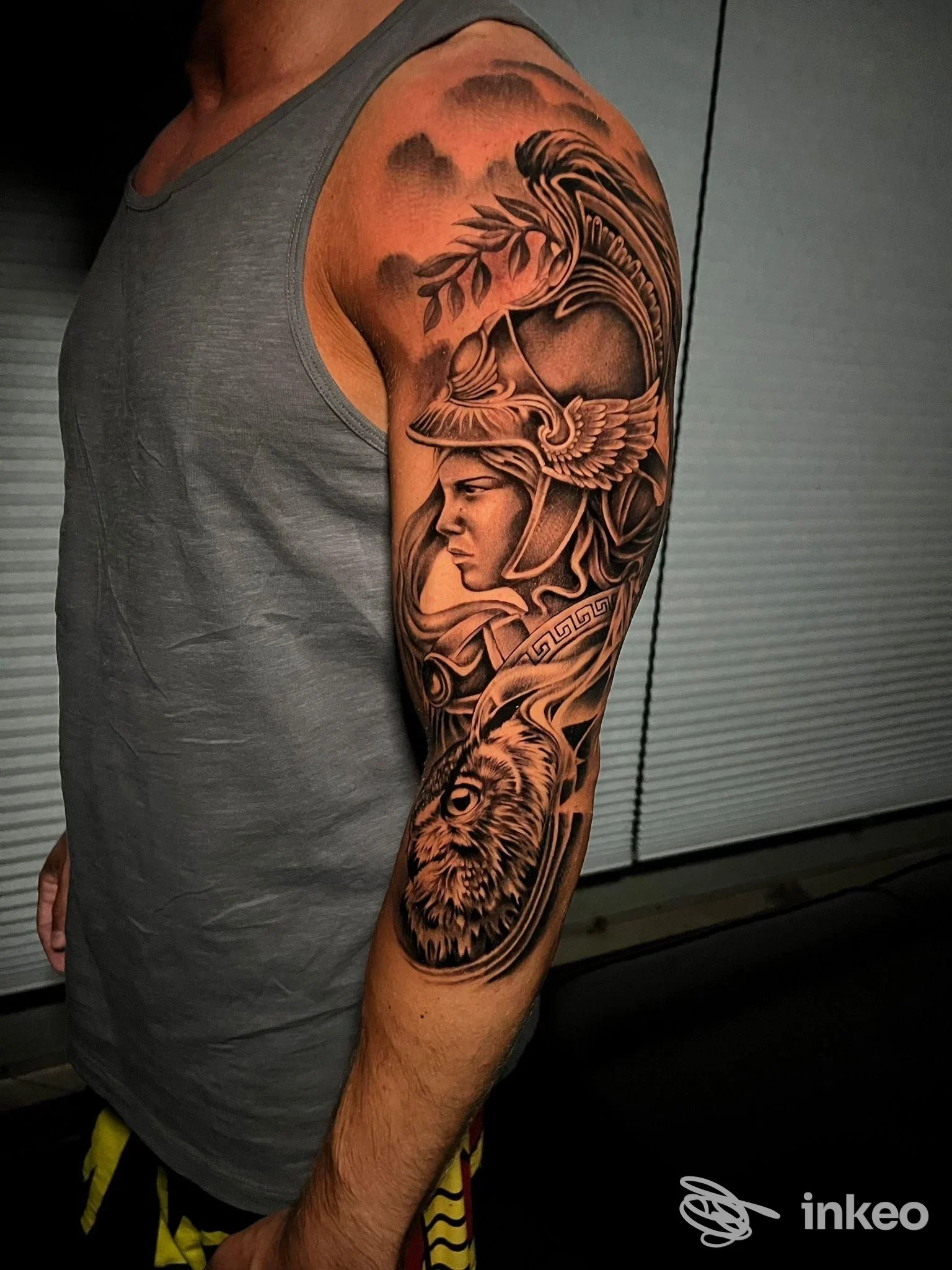 Tattoo visibile su braccio di un uomo in manichetta, sbottonato, ritratto dall’avambraccio alla spalla; stile realistico, motivi elaborati e figure, senza viso interamente visibile.