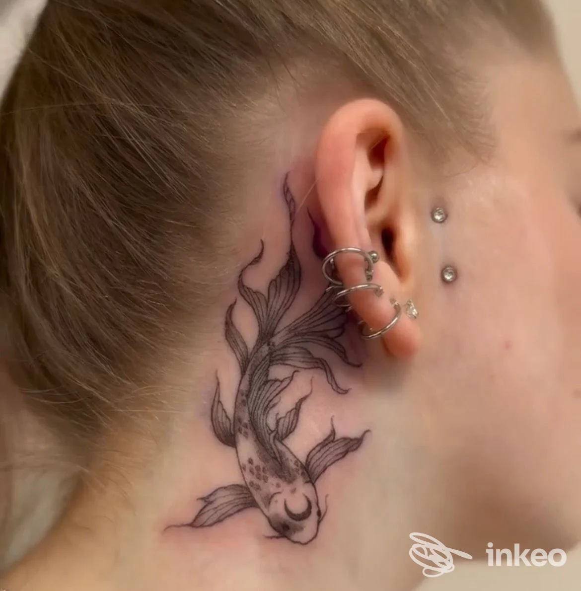 Tattoo a koi su pelle dietro l’orecchio sinistro, con riflessi neri e sfumature grigie, vicino a piercing all’orecchio; studio Modify by Venz, Pescara.