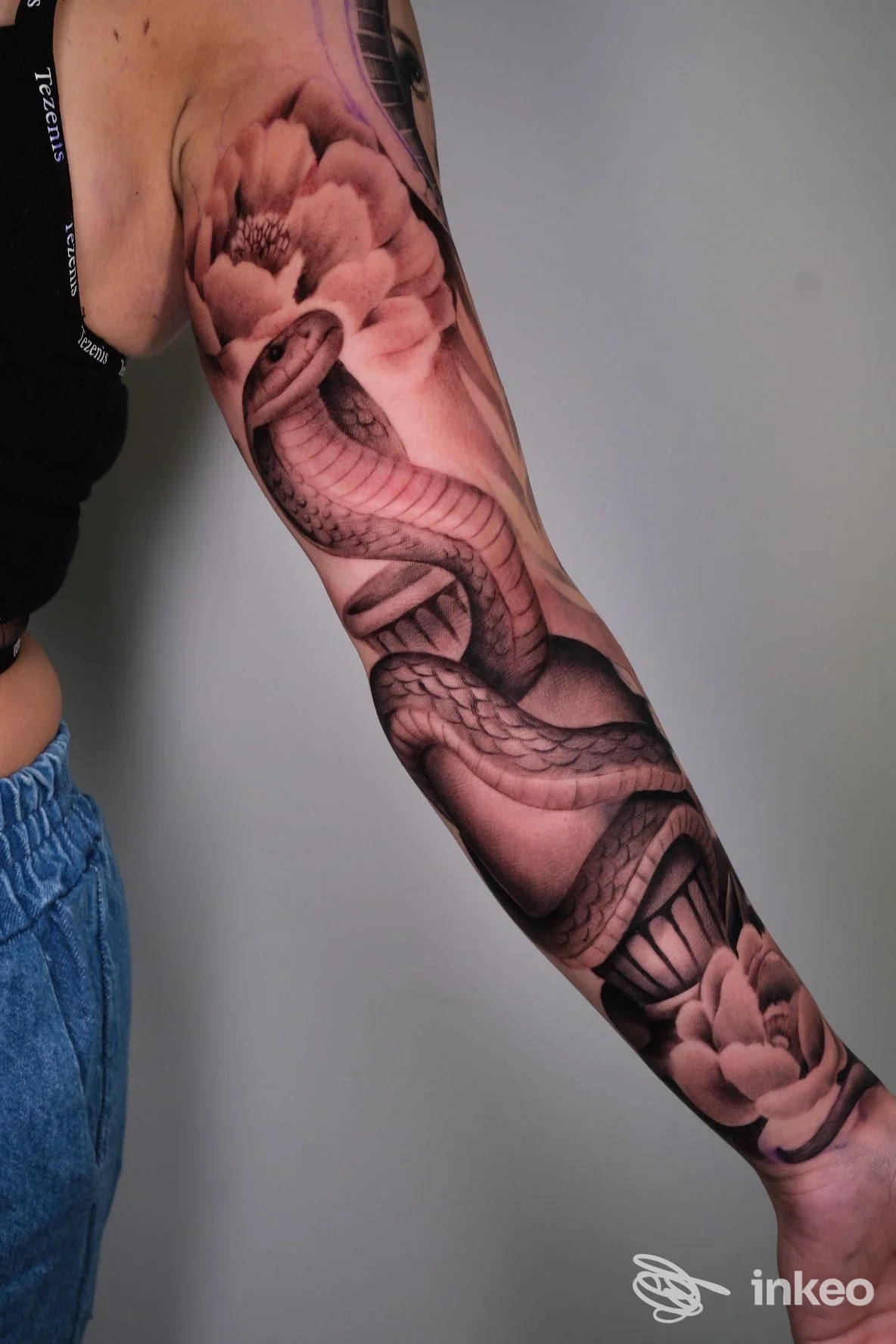 Braccio sinistro di una persona con tatuaggio realistico a manica che raffigura un serpente intrecciato tra grandi fiori, realizzato sul pele. visibile nello studio Harmonink Tattoo Shop a Chieti.