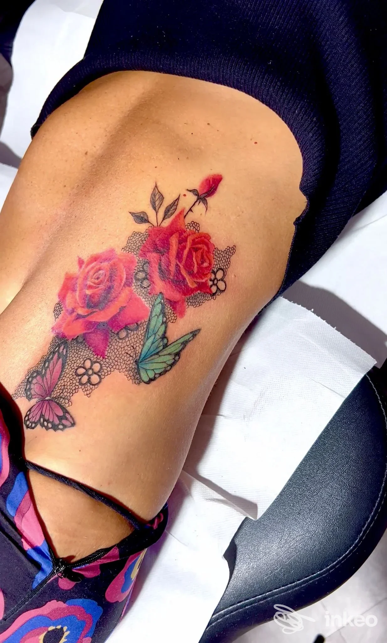 Tattoo colorata di rose e farfalle su pelle visibile sul fianco/ingresso laterale, senza elementi di interfaccia o testo visibile.