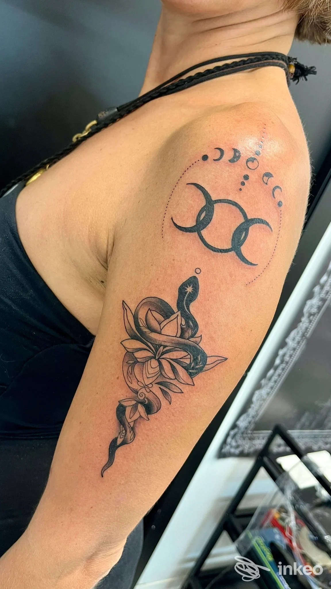 Tattoo sul braccio di una persona: fasi lunari sopra e due cerchi intrecciati, seguito da un motivo con rosa, lama e ornamenti in stile nero su pelle chiara.