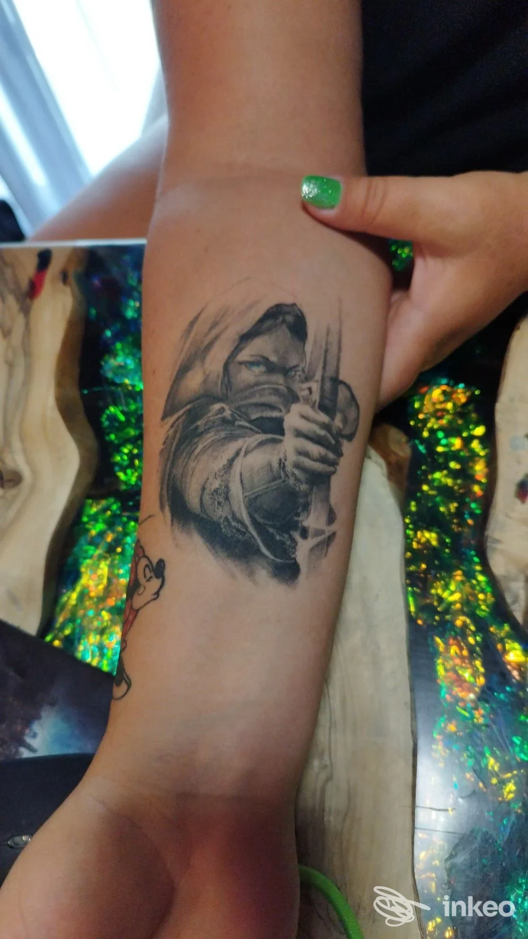 Tatuaggio realistico su avambraccio: figura incappucciata che brandisce un'arma, realizzata sulla pelle. Studio The Shark Tattoo, Chieti.