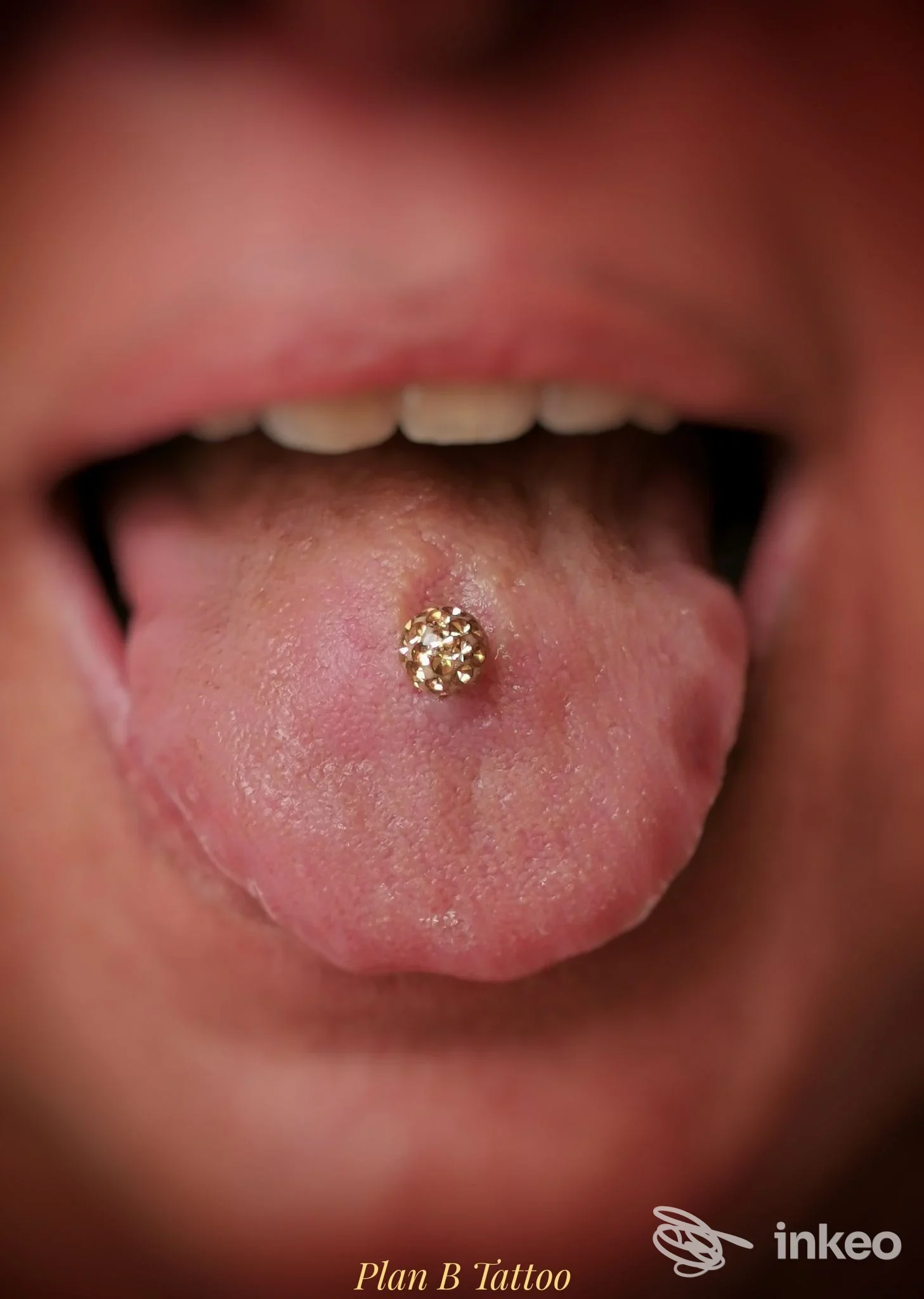 Piercing alla lingua con pallina dorata, visibile all'interno della bocca. scatto ravvicinato dal piano intraboccale.