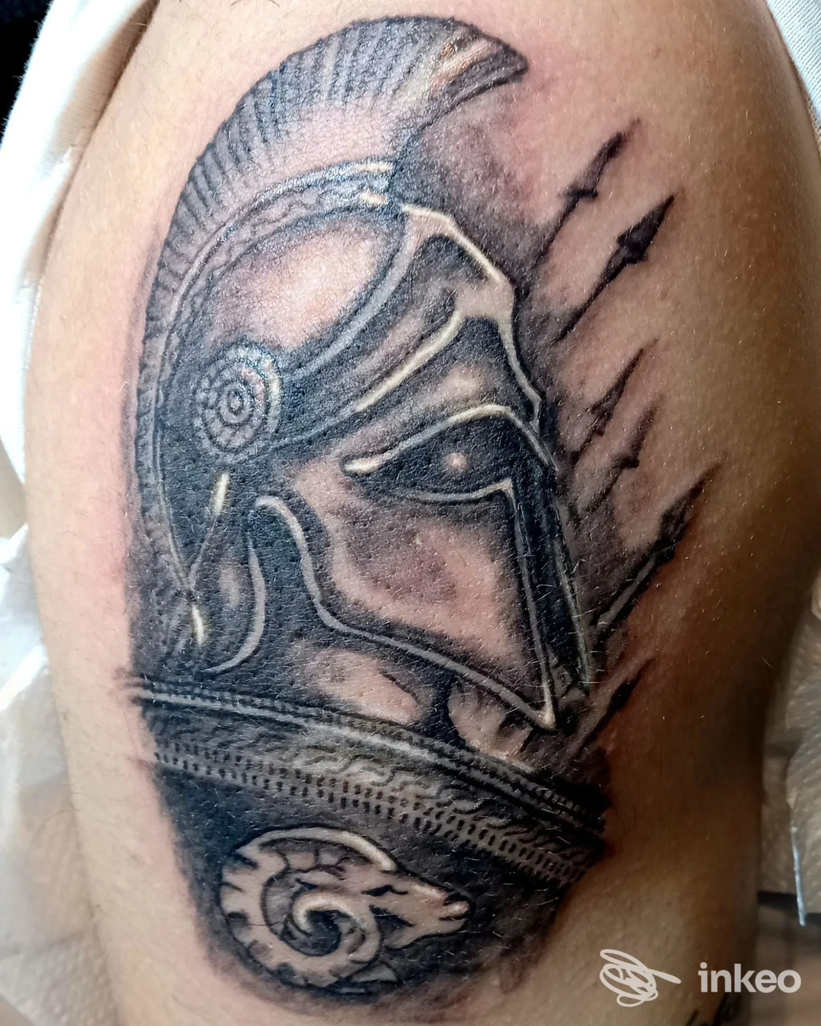 Tatuaggio su braccio ritraente un guerriero con elmo, dettaglio in bianco e nero, stile realistico, su pelle umana.