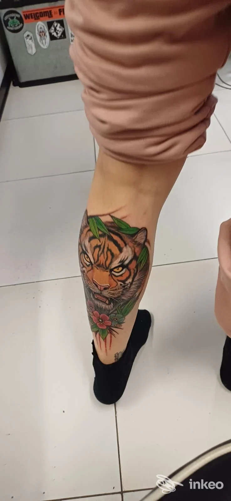 Stinco e polpaccio visibili con tatuaggio di tigre colorata, con fiori, su pelle della gamba; nessun volto visibile