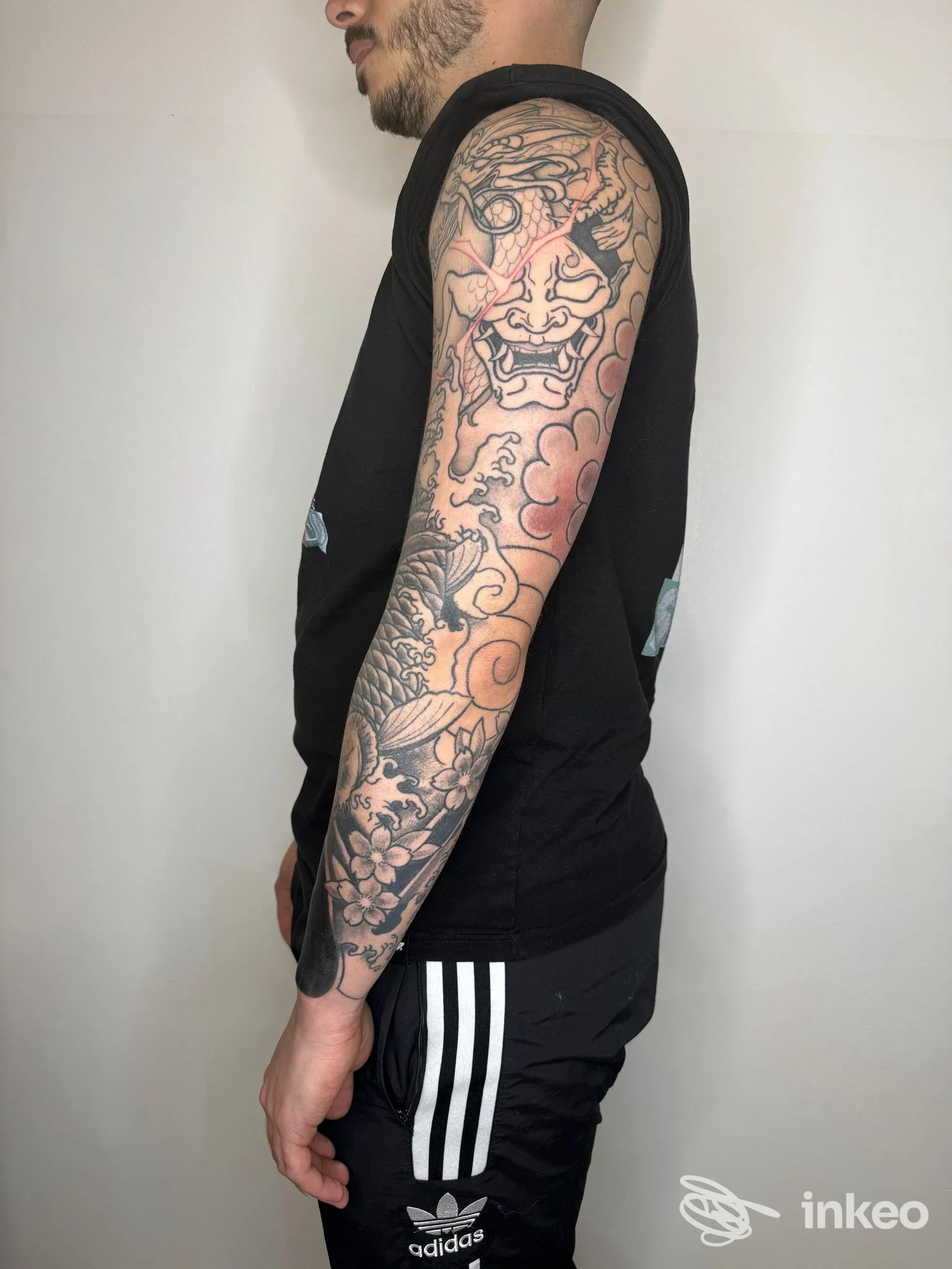 Soggetto maschile in profilo, tatuaggio a manica completa visibile sul braccio sinistro, realizzato sulla pelle, senza elementi grafici di piattaforma. Operatore: Malinkonica Tattoo Studio, Francavilla al Mare.