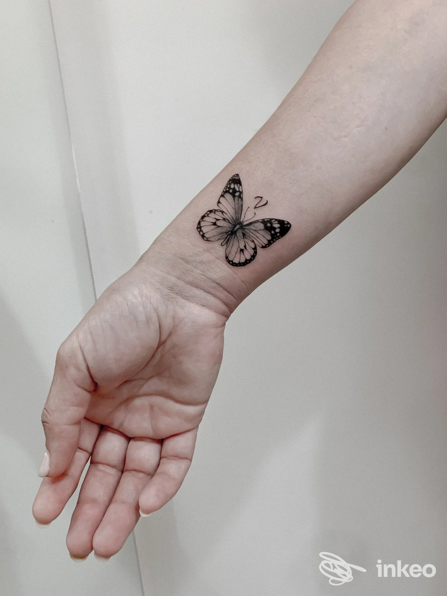 Tattoo in bianco e nero di una farfalla sul polso/avambraccio, realizzato sulla pelle di una persona; nessun volto visibile, nessuna sovrapposizione; stile line work con dettagli netti.