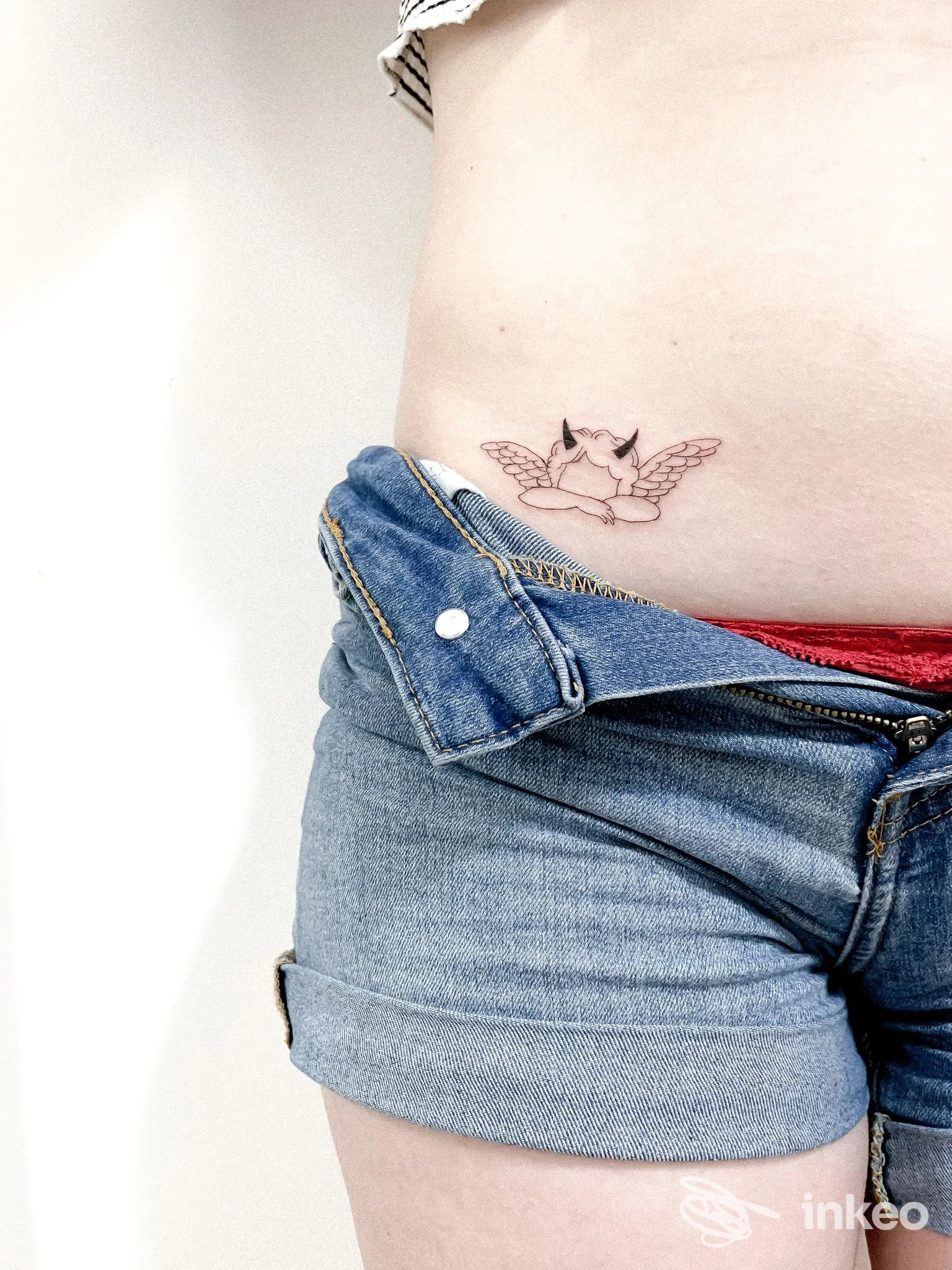 Piccolo tattoo al fianco raffigurante una creatura alata, visibile su una pancia/addome di una persona, indossa shorts di jeans.