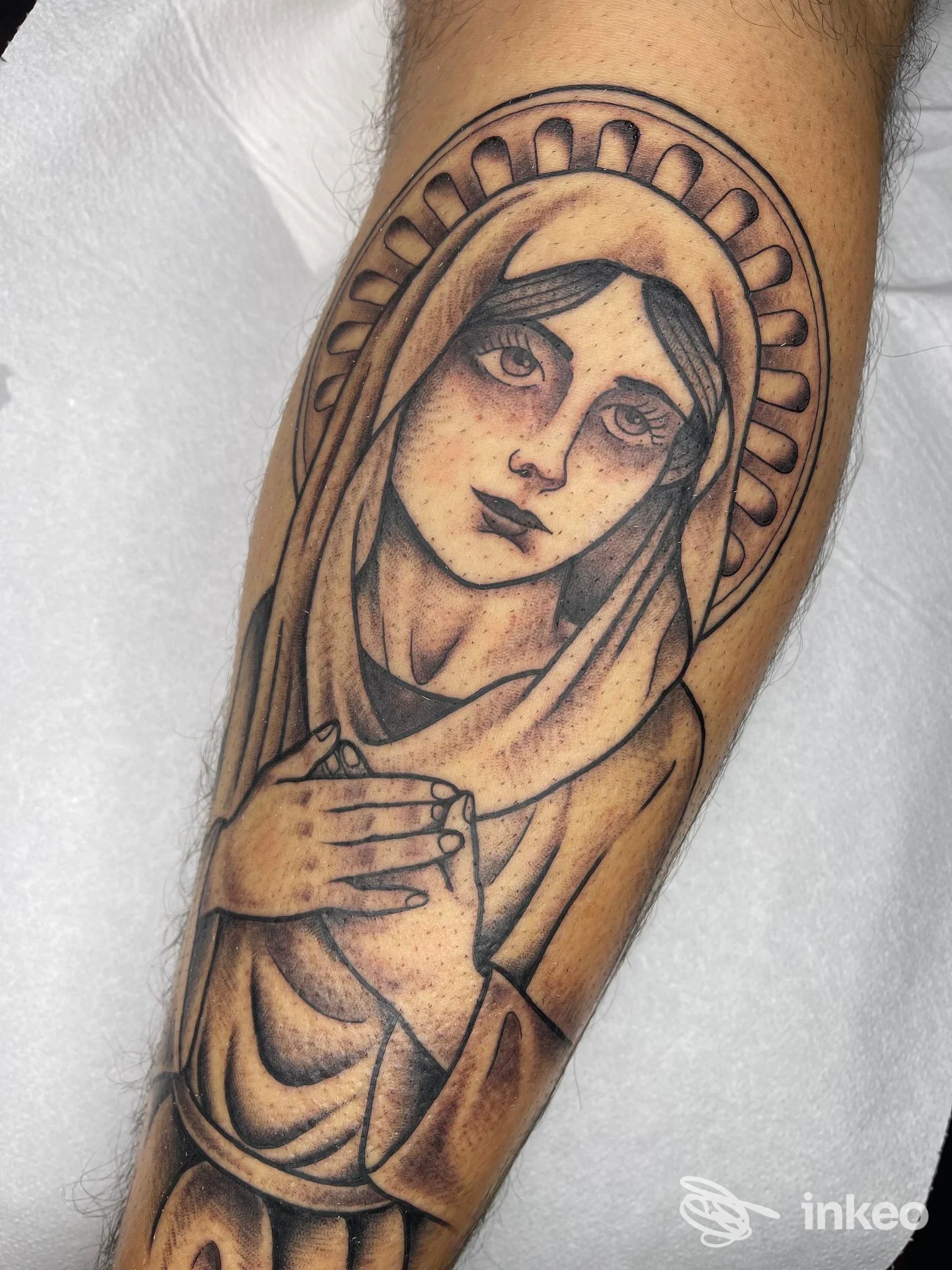 Tattoo religioso raffigurante una figura femminile sacra sulla parte inferiore del braccio, stile linee nere e tonalità terrose, realizzata su pelle.