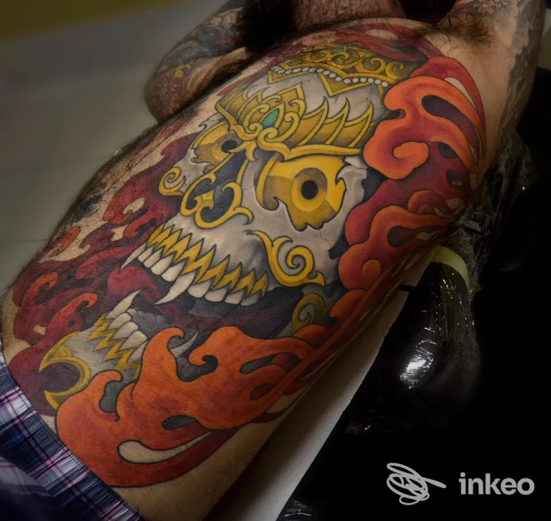 Tatuaggio di grande braccio raffigurante un teschio stilizzato con fuoco arancione e dettagli colorati, eseguito sulla pelle in uno studio di tatuaggi a Pescara.
