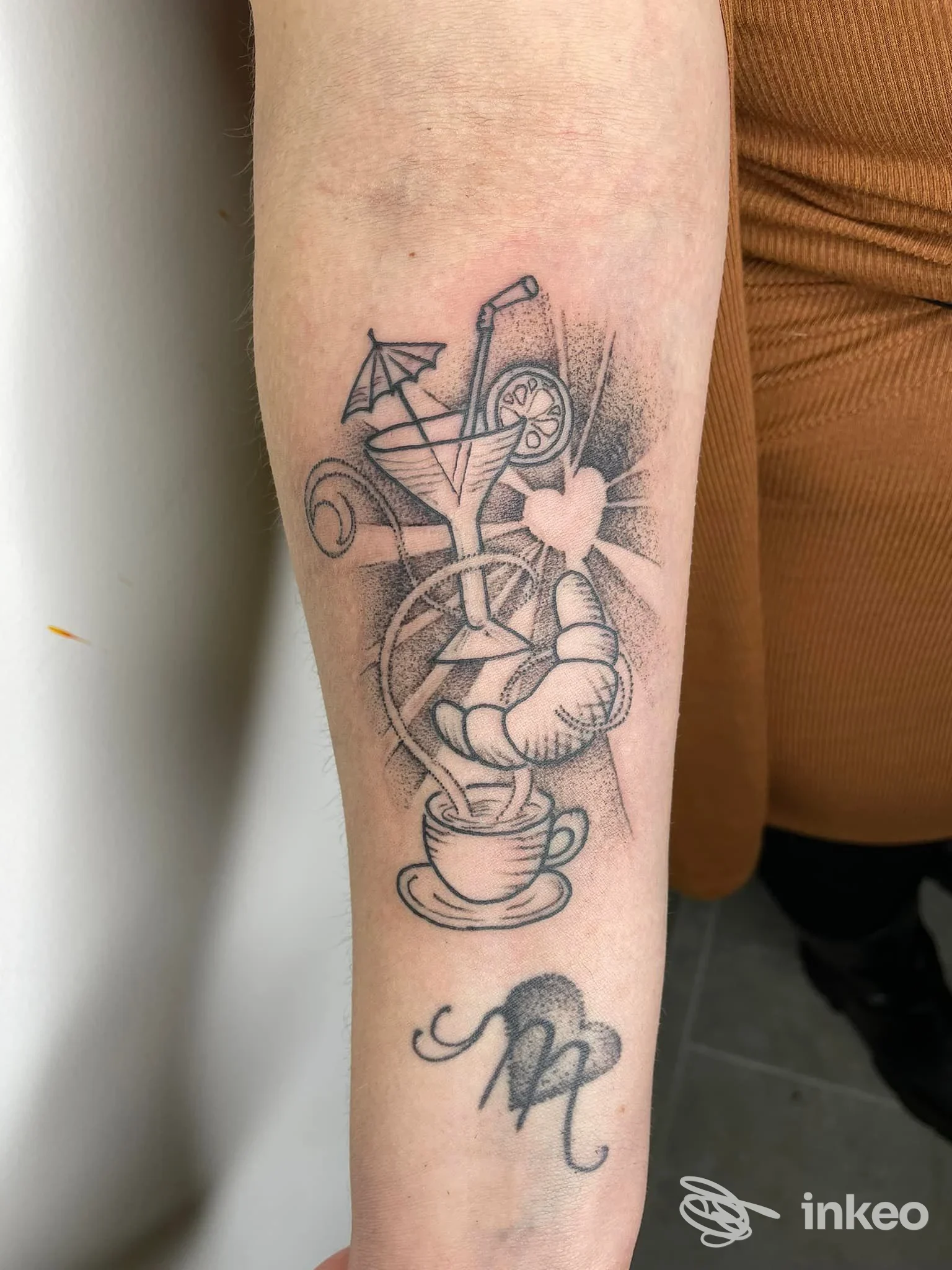 Tattoo frontale su avambraccio raffigurante un drink con cannuccia e fiori, disegno in stile linework con sfondo sfumato; firma della pelle visibile e dettagli nitidi. Studio Cuore Nero, Pescara.