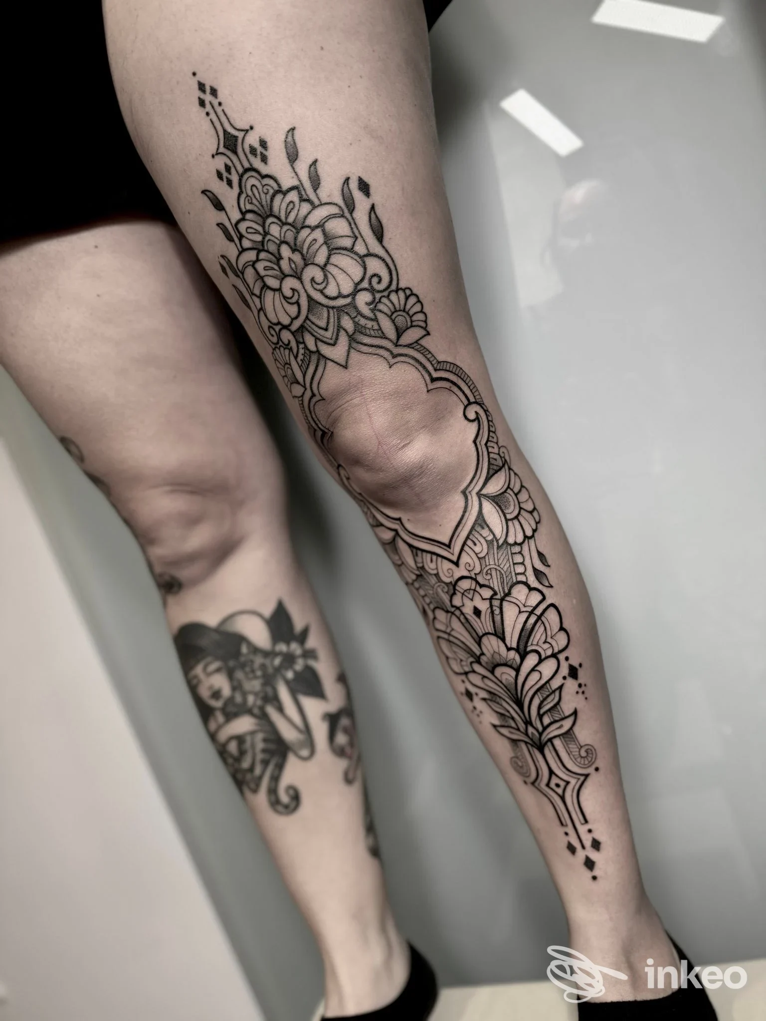 Tattoo ornato su gamba, disegno lineare e floreale che segue la tibia e lo stinco, eseguito su pelle reale.