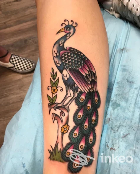 Pavone colorato tatuato sull'avambraccio sinistro, dettagliato e ben definito, con piume e colori vivaci.