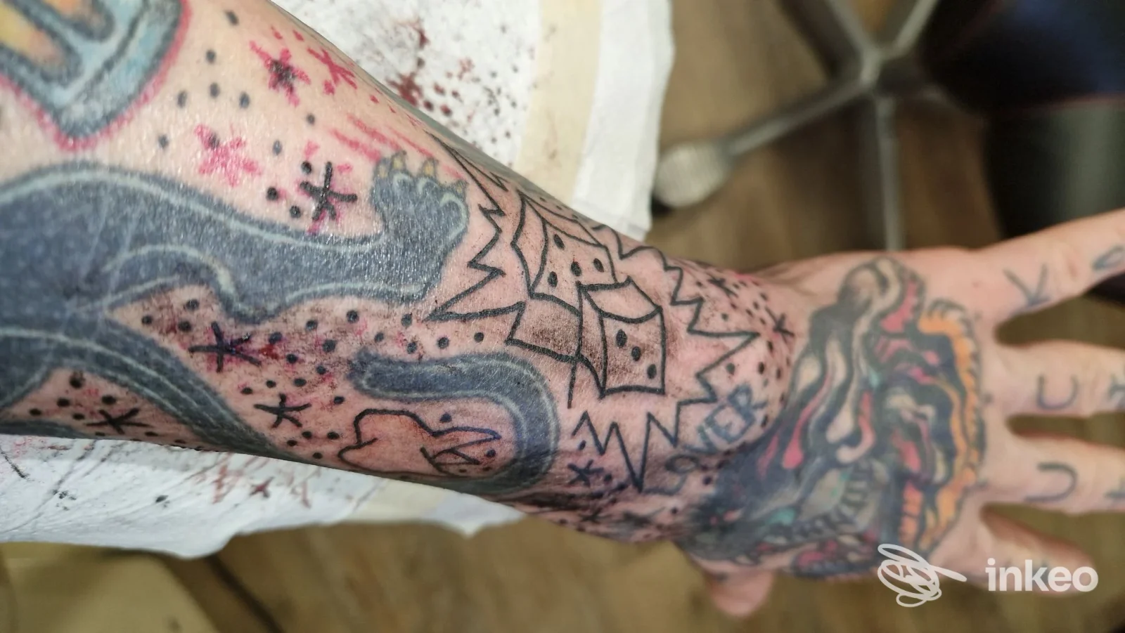 Brazo sinistro con tattoo visibile: motivi neri e riempimenti colorati, braccio appoggiato su una superficie chiara, senza viso.