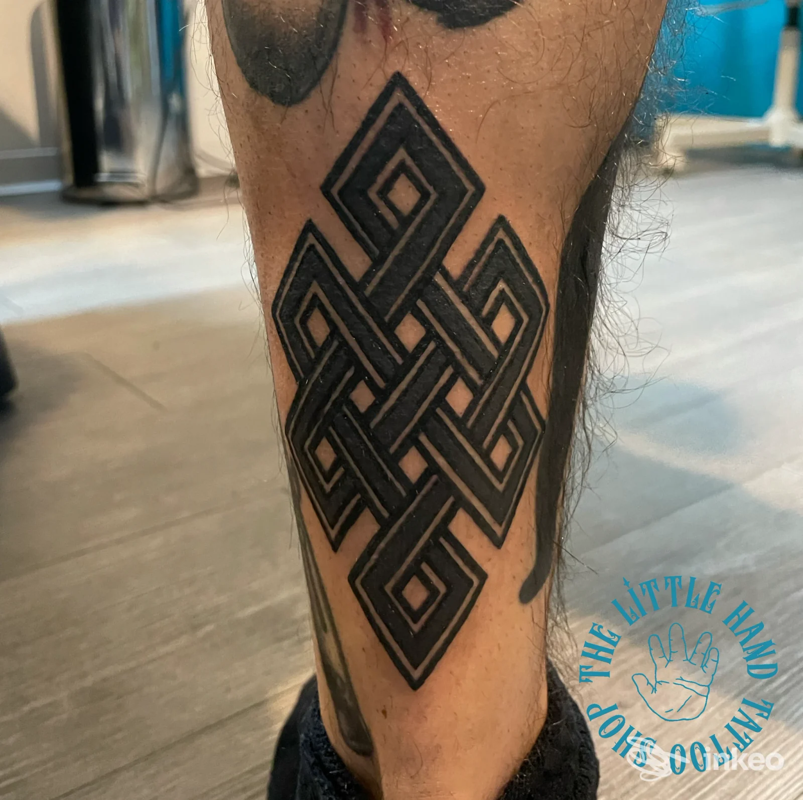 Tattoo geometrico stilizzato a motivo intrecciato sulla parte inferiore della gamba, inchiostrato con linee nere ben definite su pelle chiara, nessun volto visibile.