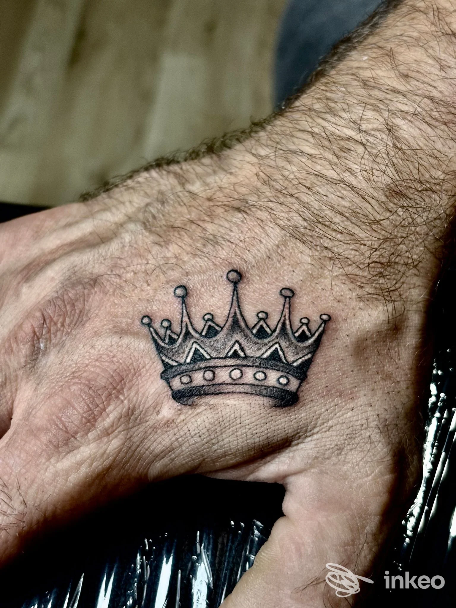 Tatuaggio di una corona nera su pelle chiara, visibile sul dorso della mano; studio Open Eyes, Lanciano.