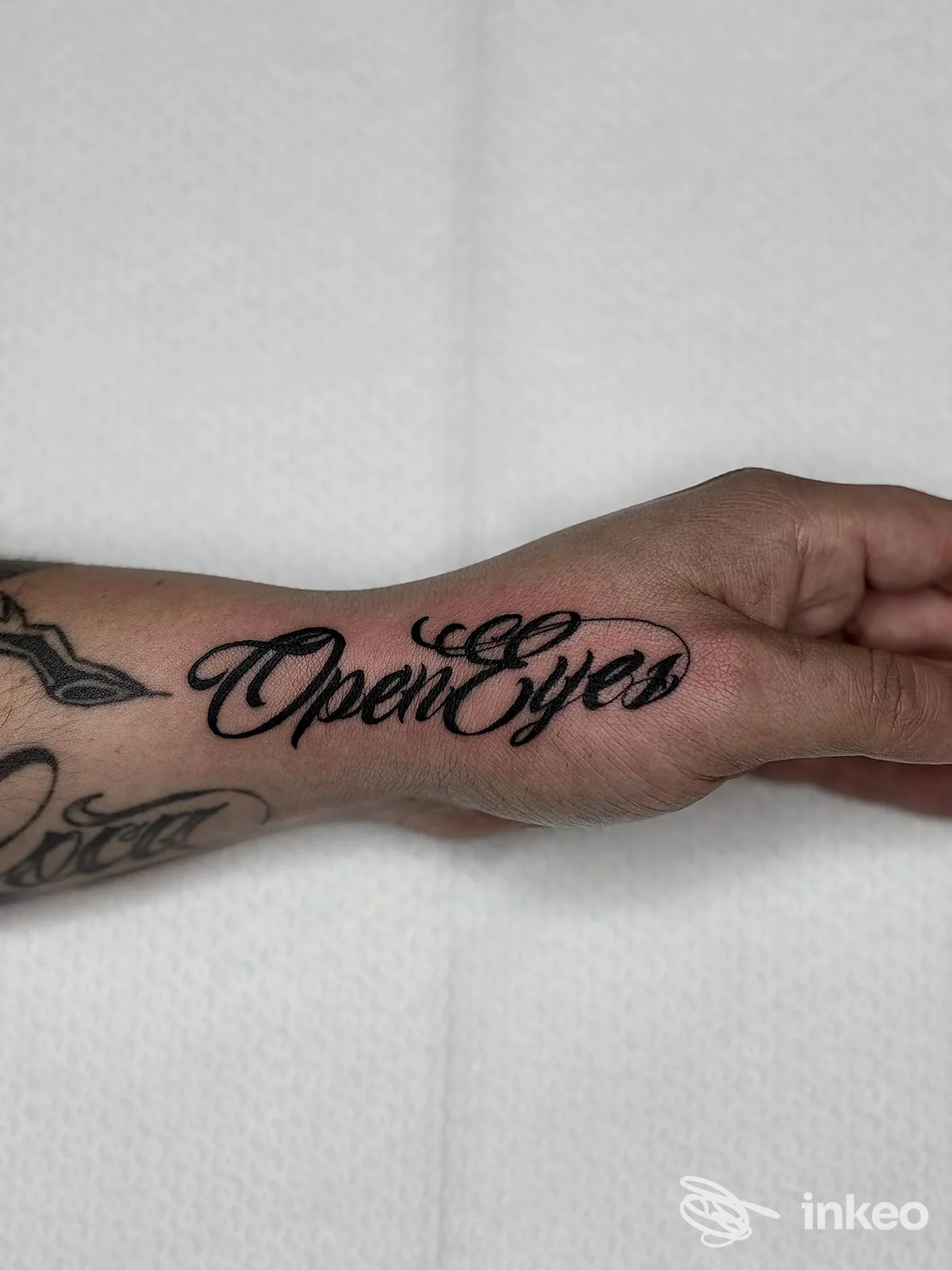 Mano con tatuaggio in stile script nero che dice Open Eyes, inciso sulla pelle
