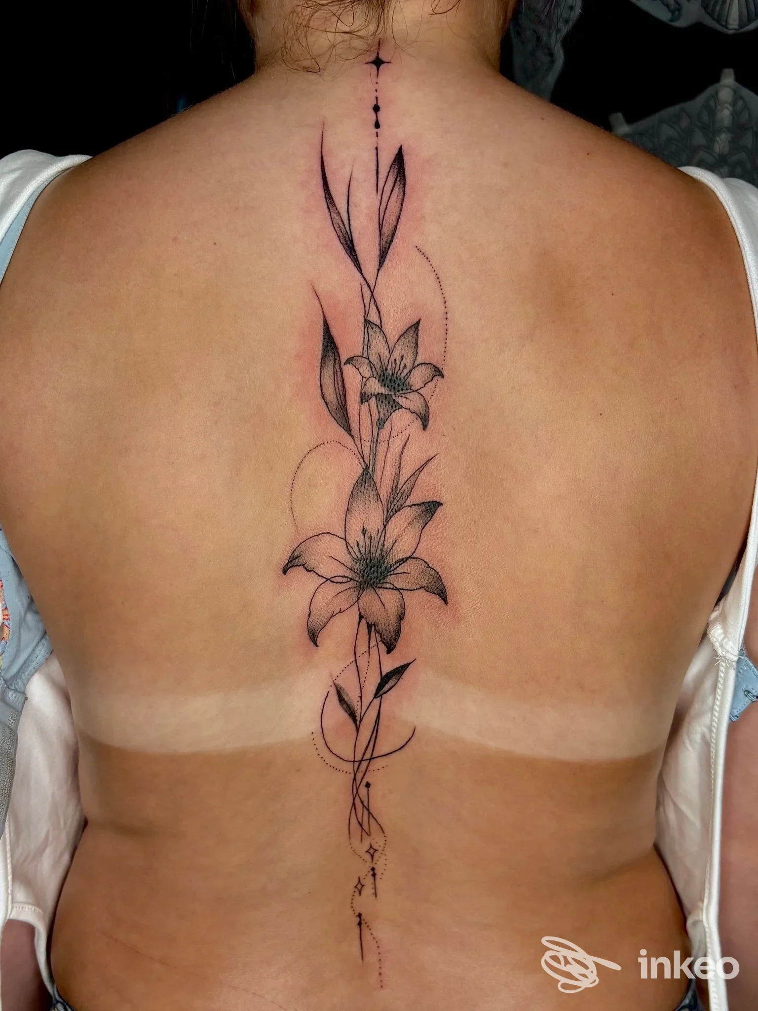 Tattoo verticale di fiori lungo la linea della schiena, realizzato direttamente sulla pelle, senza elementi visivi di interfacce social o immagini estranee.
