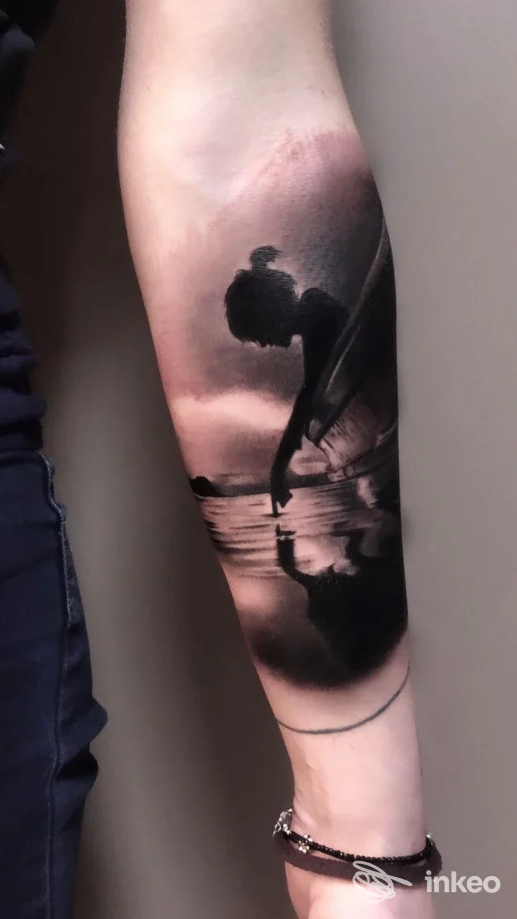 Tatuaggio realistico in bianco e nero sull'avambraccio a Pescara presso Simone Liberatore Tattoo Studio: figura riflessa sull'acqua al tramonto.