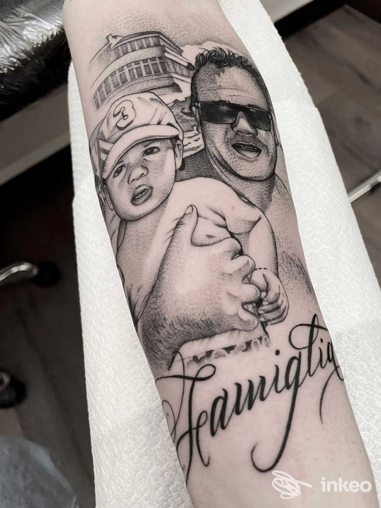 Tattoo raffigurante due volti e una scritta in corsivo sull’avambraccio; stile realistico in bianco e nero realizzato sul tessuto della pelle.