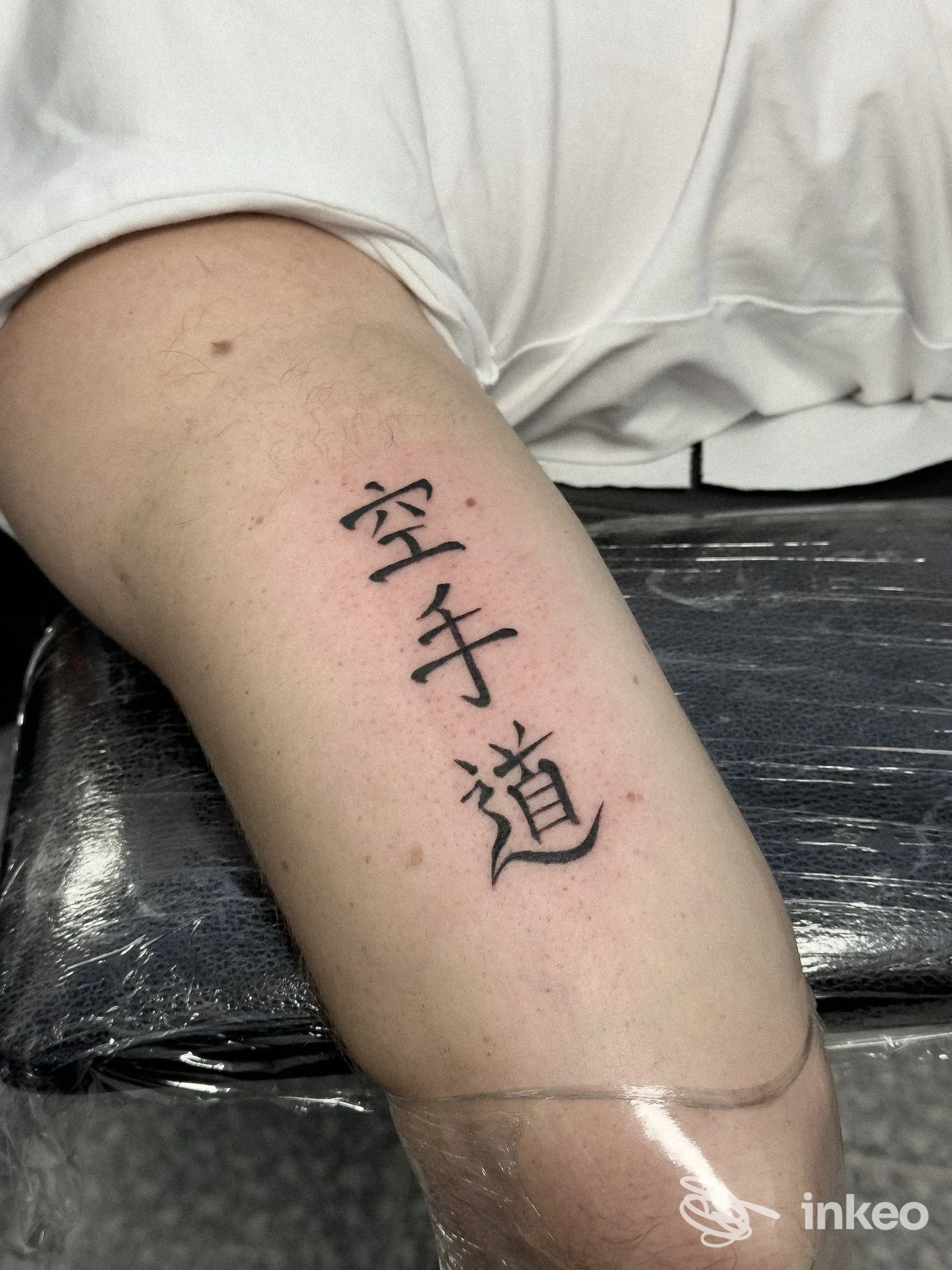 Tattoo visibile sull'avambraccio sinistro, stile kanji/ideogrammi neri disegnato sulla pelle, senza volto visibile; scatto ravvicinato in studio, nulli elementi di interfaccia o testo esterno all'opera. Studio Indelebile Tattoo Shop, Cepagatti (PN).