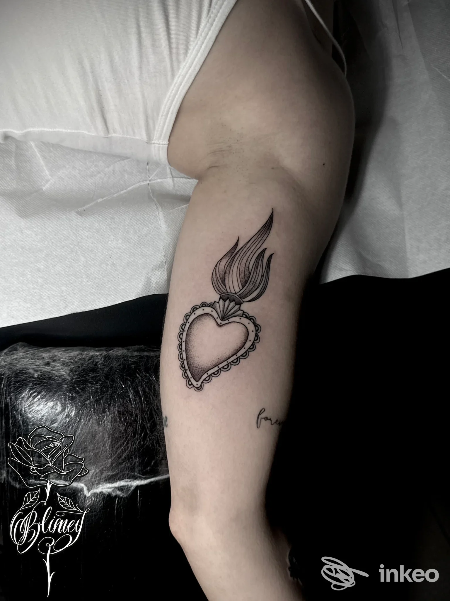 Braccio di una persona con tatuaggio visibile: cuore ornato con bordo a catena e fiamma sopra, in stile disegno lineare. Studio Blimey Tattoo, Avezzano.