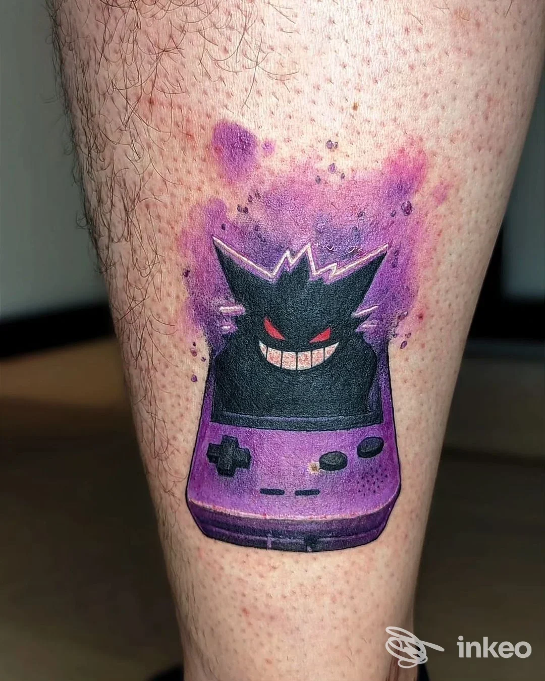 Tattoo colorato su polpaccio raffigurante una console di gioco viola con personaggio nero a forma di mascotte, contorno sfumato viola sullo sfondo.