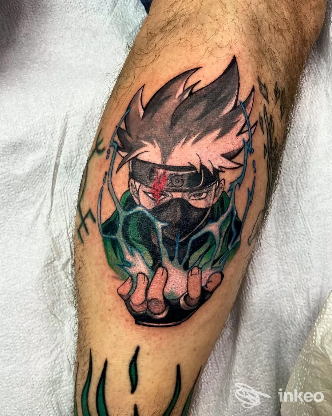 Avambraccio con tatuaggio colorato ispirato a un personaggio anime, raffigurante una figura con maschera, mani in primo piano e dettagli grafici neon, eseguito sulla pelle.
