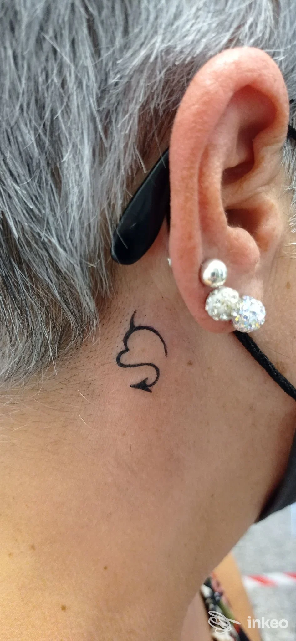 Orecchio destro con piercing e piccolo tatuaggio nero vicino al collo, scatto ravvicinato su pelle esposta, senza watermark o testo promozionale.