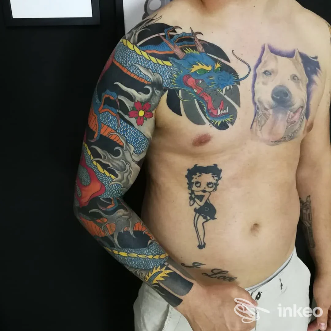 Parte del torace e del braccio sinistro di uomo con tatto artistico: dragone blu e rosso sull’avambraccio e ritratto di cane sul petto.