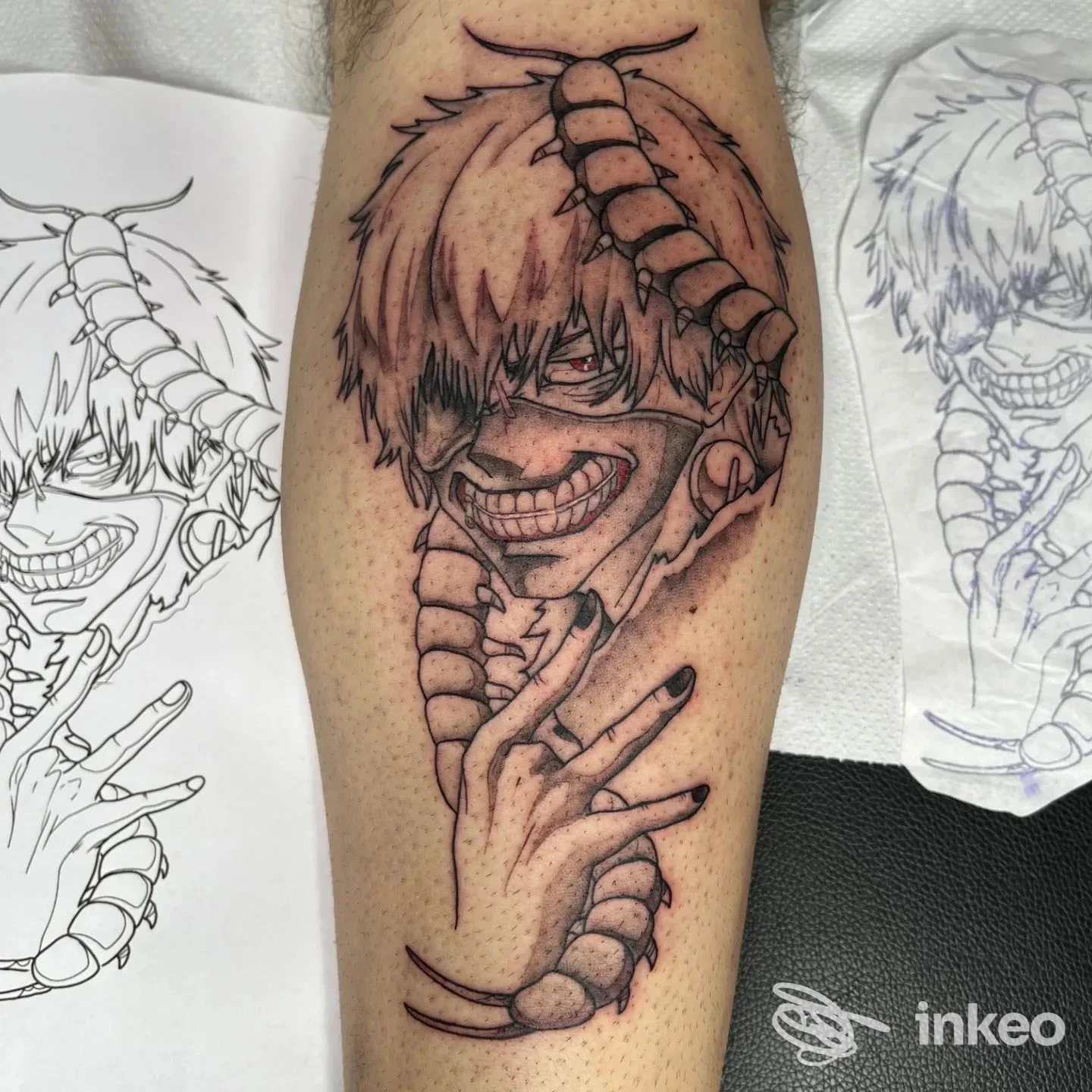 Tatuaggio su pelle raffigurante un character con espressione intensa, con contorni scuri e sfumature rosse, visibile sulla gamba/avambraccio; al retro si vedono schizzi preparatori.