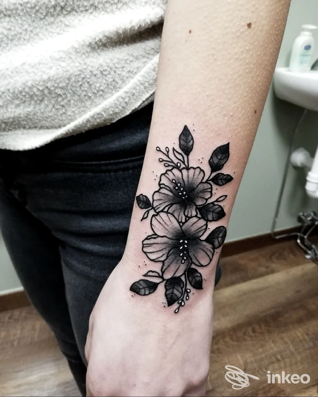 Tattoo floreale su avambraccio di una persona, inchiostro nero con fiori e foglie, foto in studio.