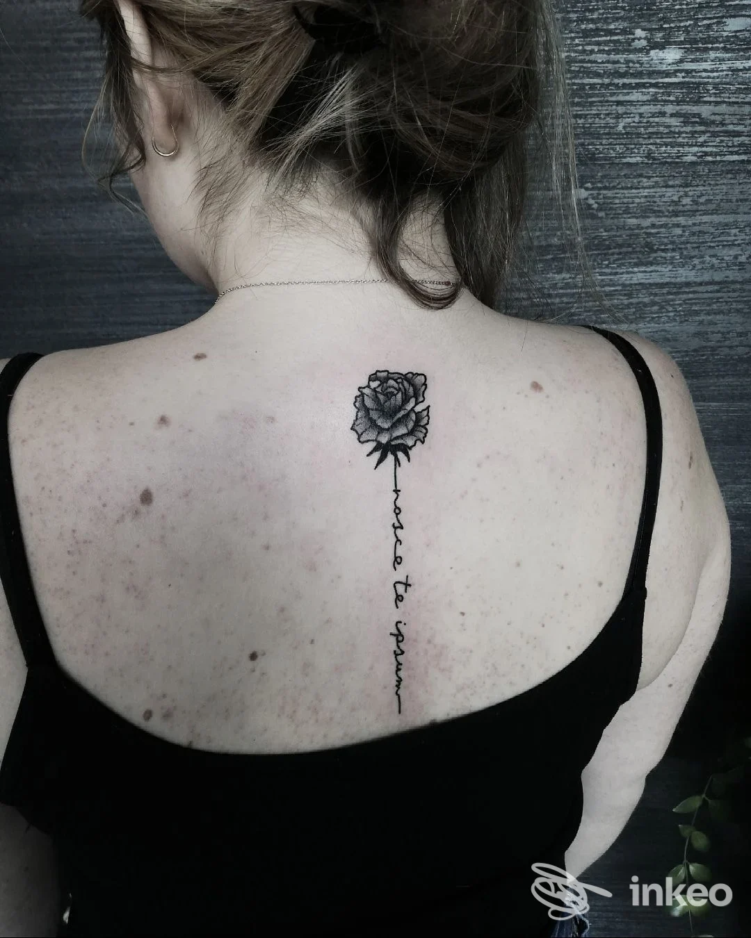 Tattoo sul dorso di una persona: una rosa nera con scritte che scendono lungo la schiena, visibile tra le spalle, eseguito presso Maison Le Noir Tattoo Parlour a Pineto.
