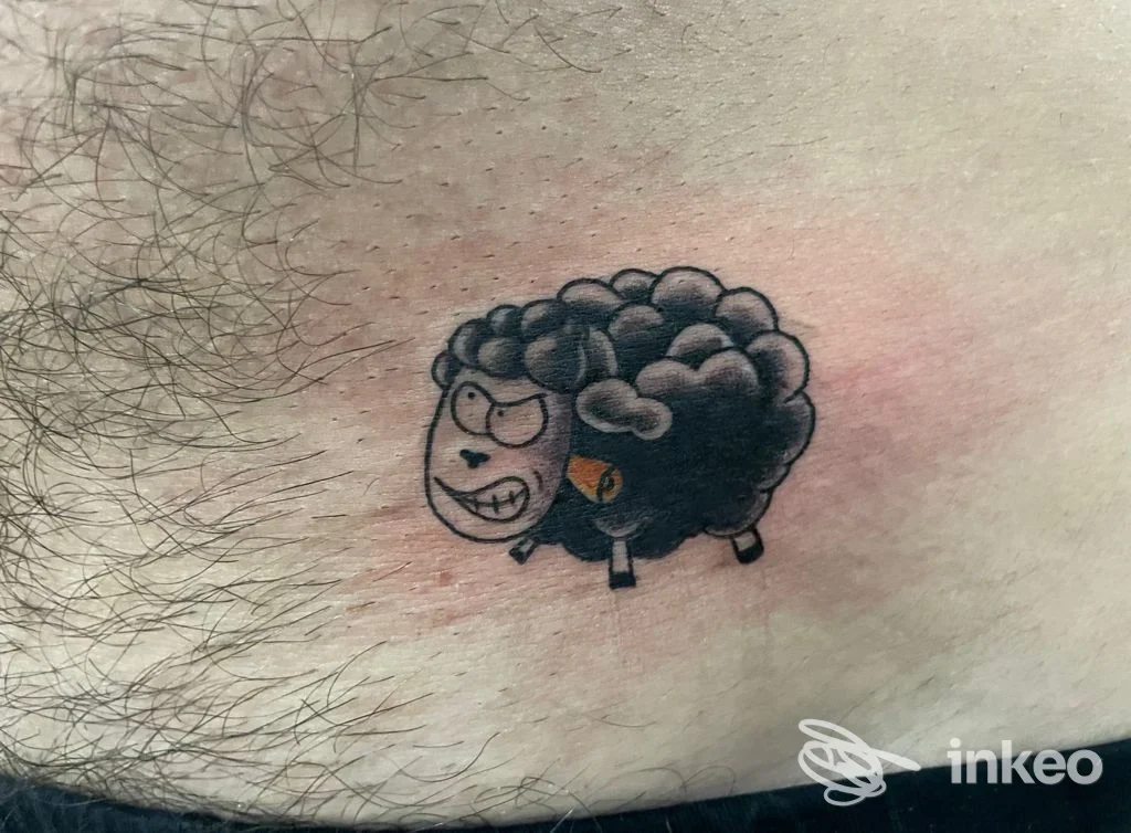Tattoo su pelle raffigurante una pecora cartoonesca con peli scuri e contrasto rosa attorno; realizzato sul polpaccio, stile cartoon.