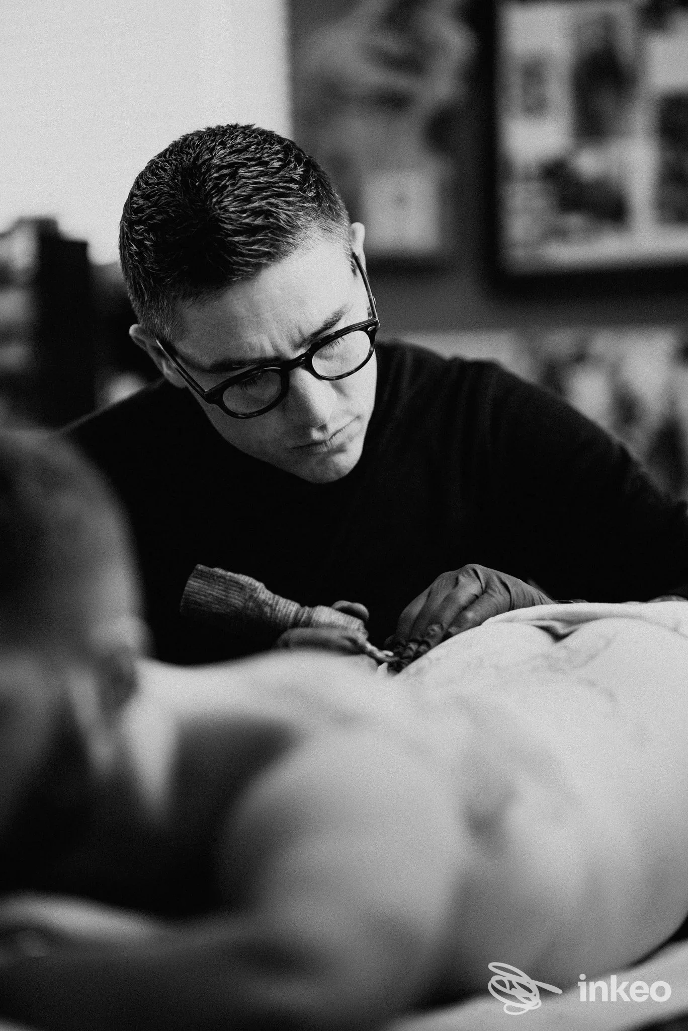 Procedura di tatuaggio in corso su un modello, artigiano con occhiali lavora su una schiena, nello studio Millo Tattoo Studio a Giulianova, bianco e nero.
