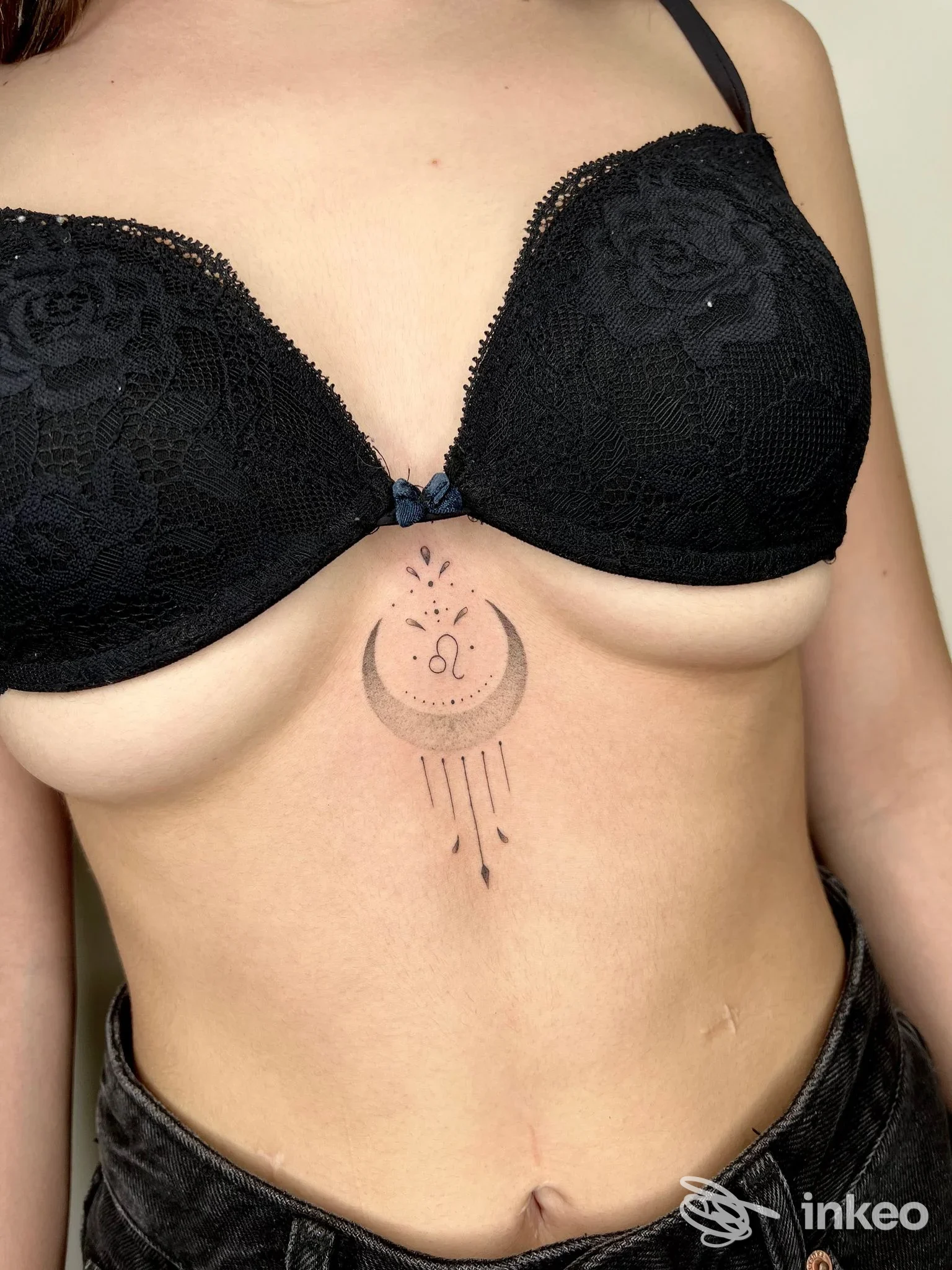 Tattoo visibile sul fianco/torace di una persona, disegno di luna stilizzata con puntini e linee pendenti sotto, carnagione chiara, indossa reggiseno nero. Studio Foxink, Vasto.