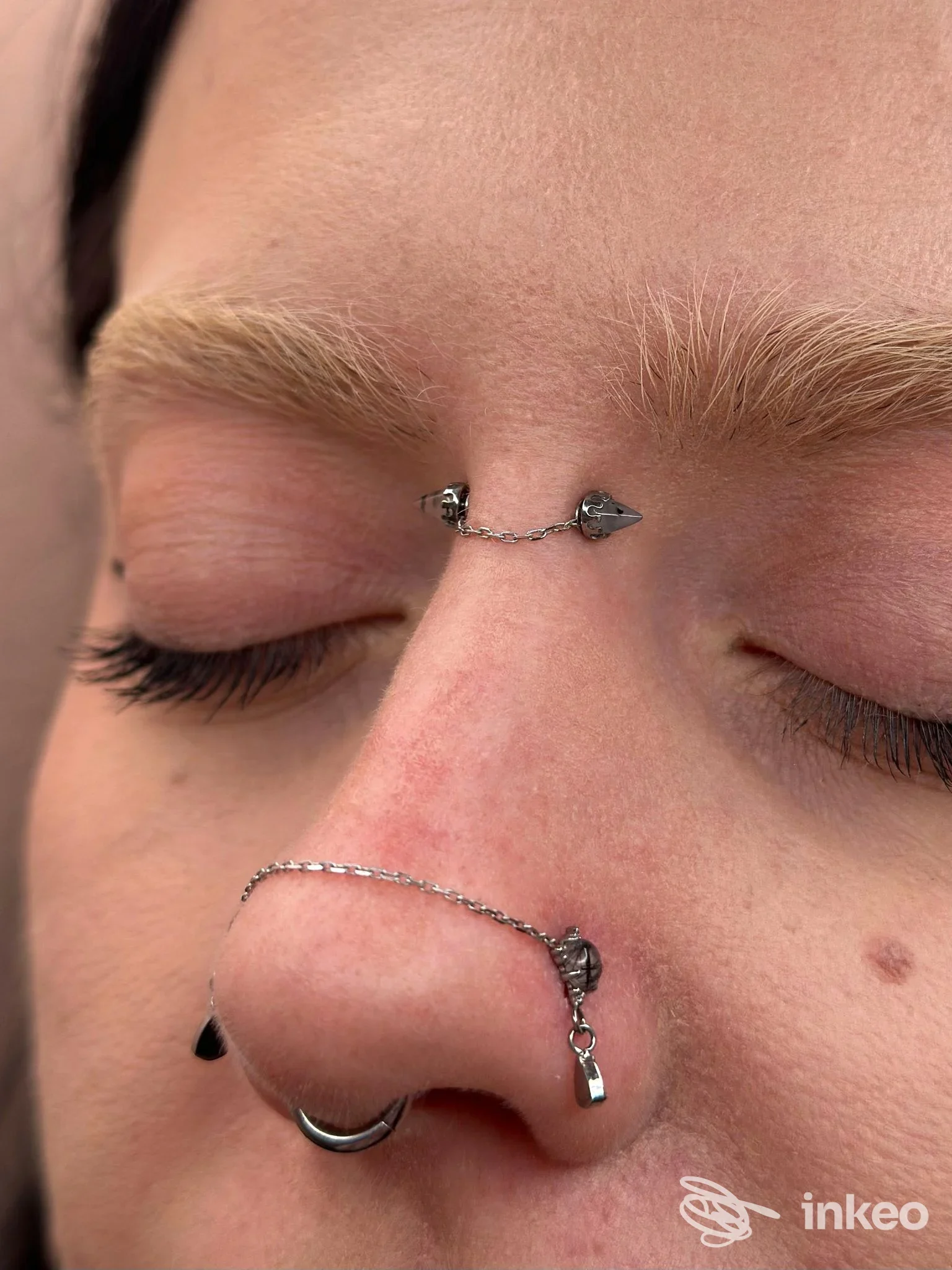 Primo piano del volto con piercing al naso e catena sull'ala del naso e sull'osso nasale, mostra piercing multipli. studio Ellylù, Pescara.