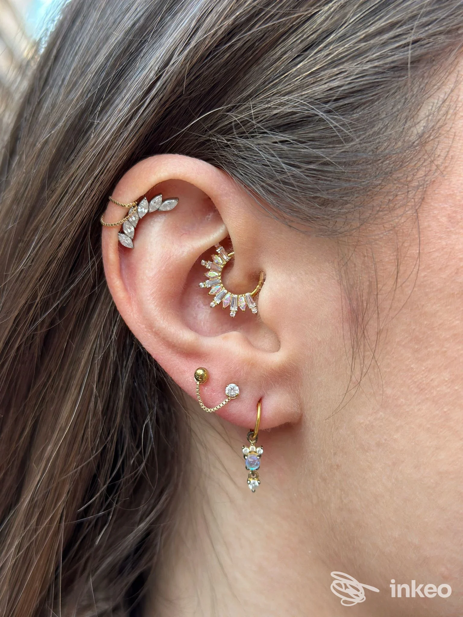 Orecchini multipli all'orecchio, con piercing dorati e gioielli a forma di gocce, indossati su più fori dell'orecchio in primo piano.